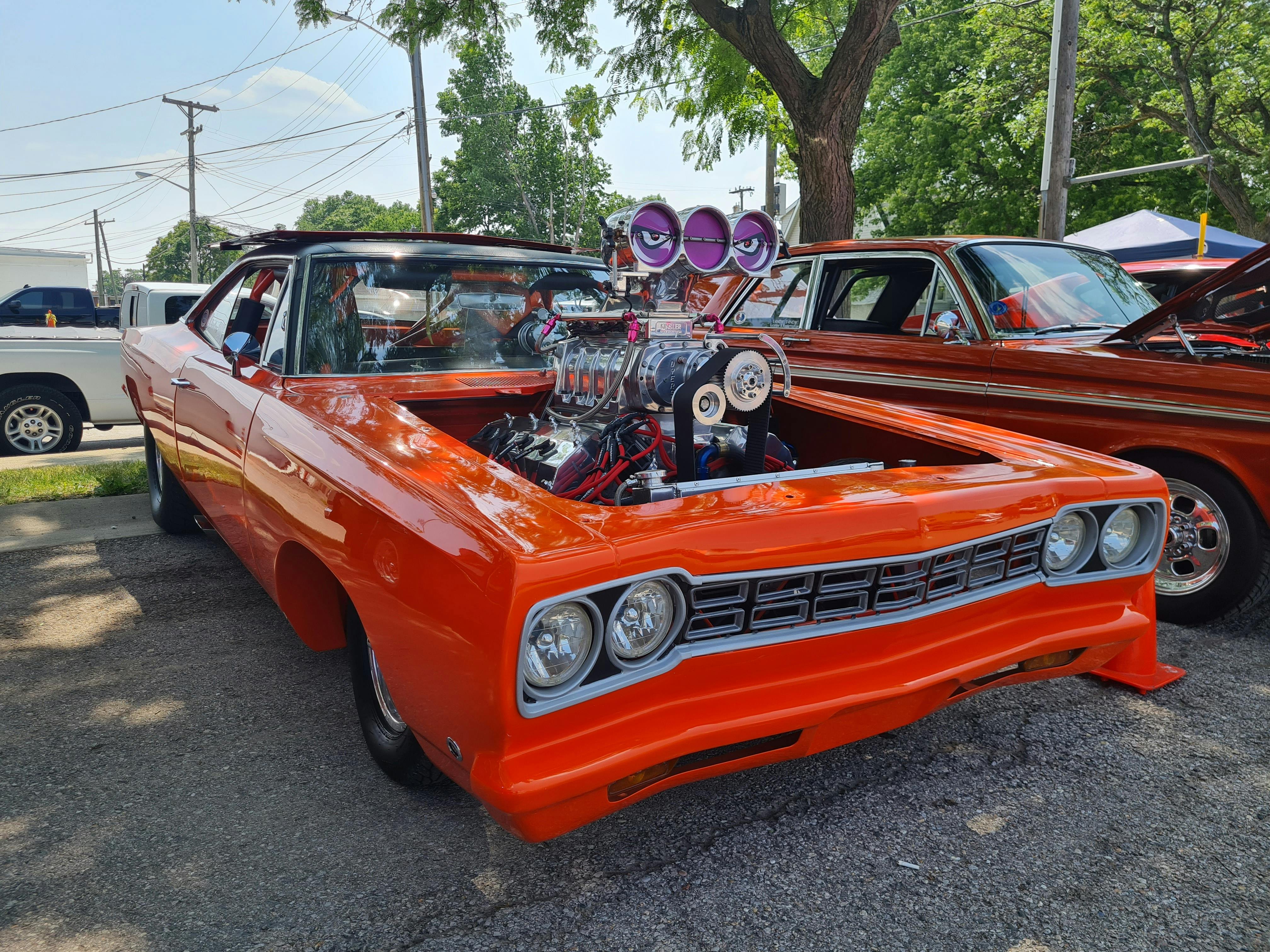 Dodge charger 1967 orange sans capot exposant le moteur qui possède gros blower violet avec de yeux